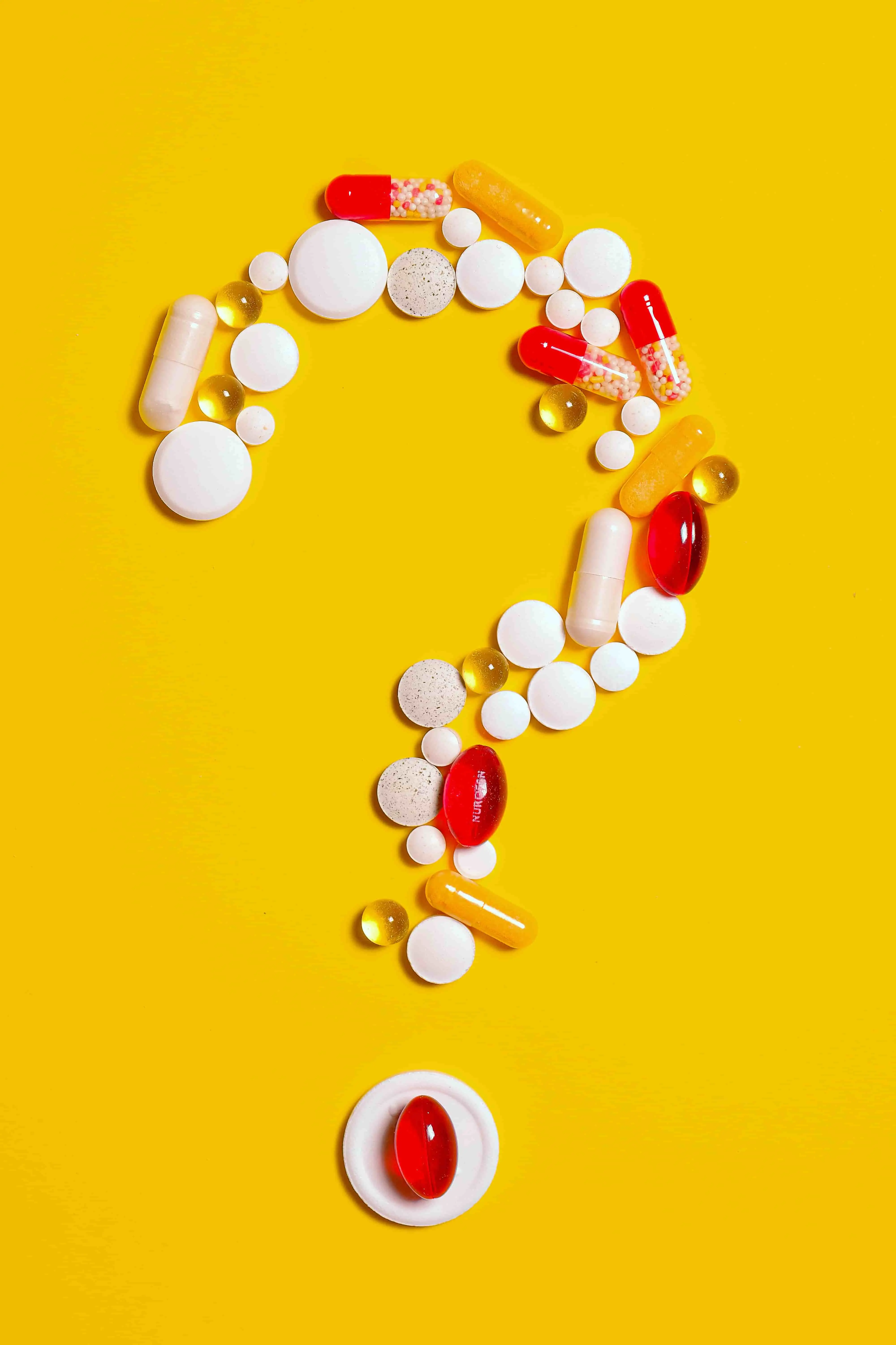 Image of an assortment of tablets and capsules arranged in the shape of a question mark on a yellow background